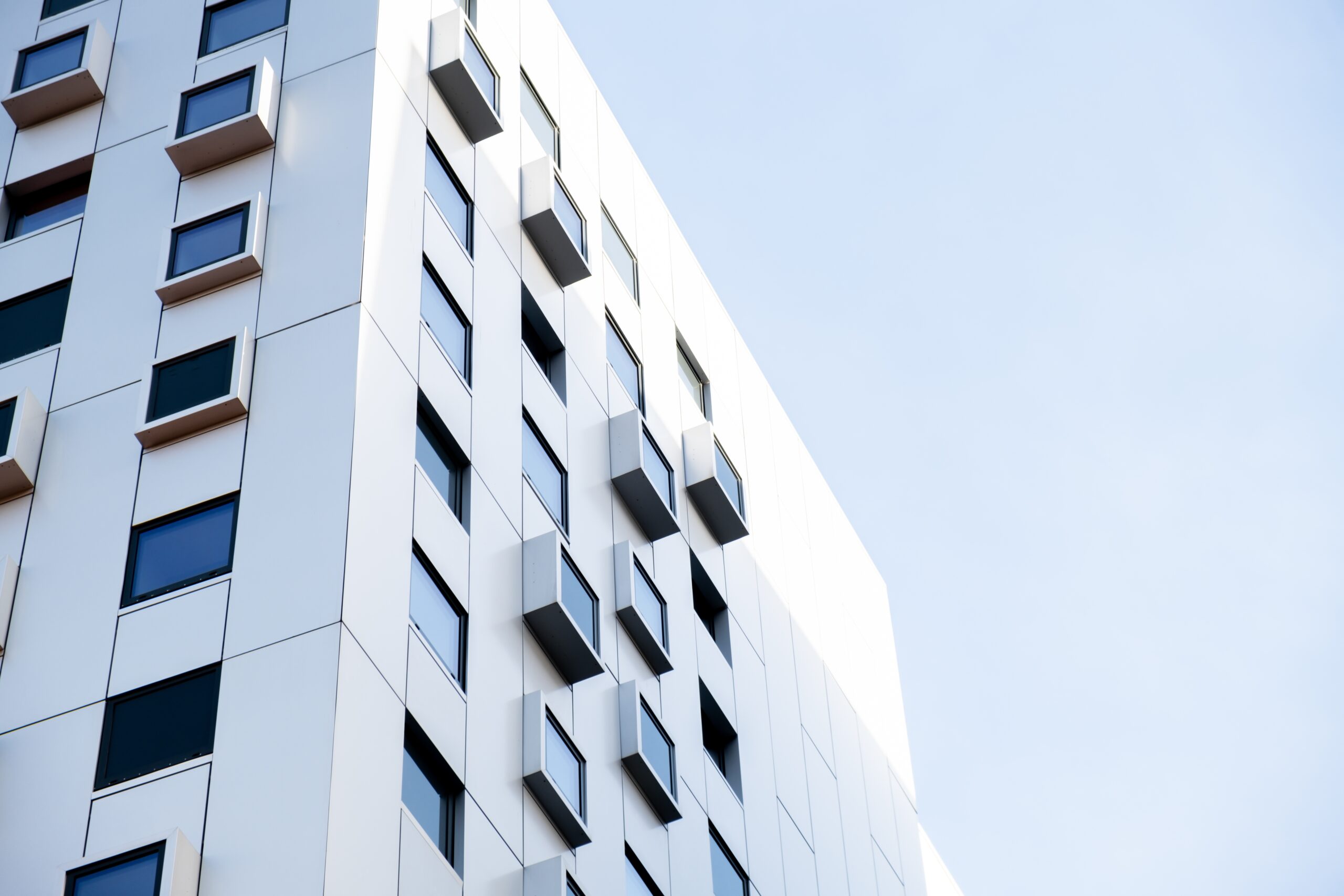 Modern wit gebouw met vierkante ramen. Appartementencomplex met meerdere verdiepingen. Minimalistisch, stijlvol wooncomplex. Gevels van een modern kantoorgebouw. Textuurpatroon aan de buitenkant.