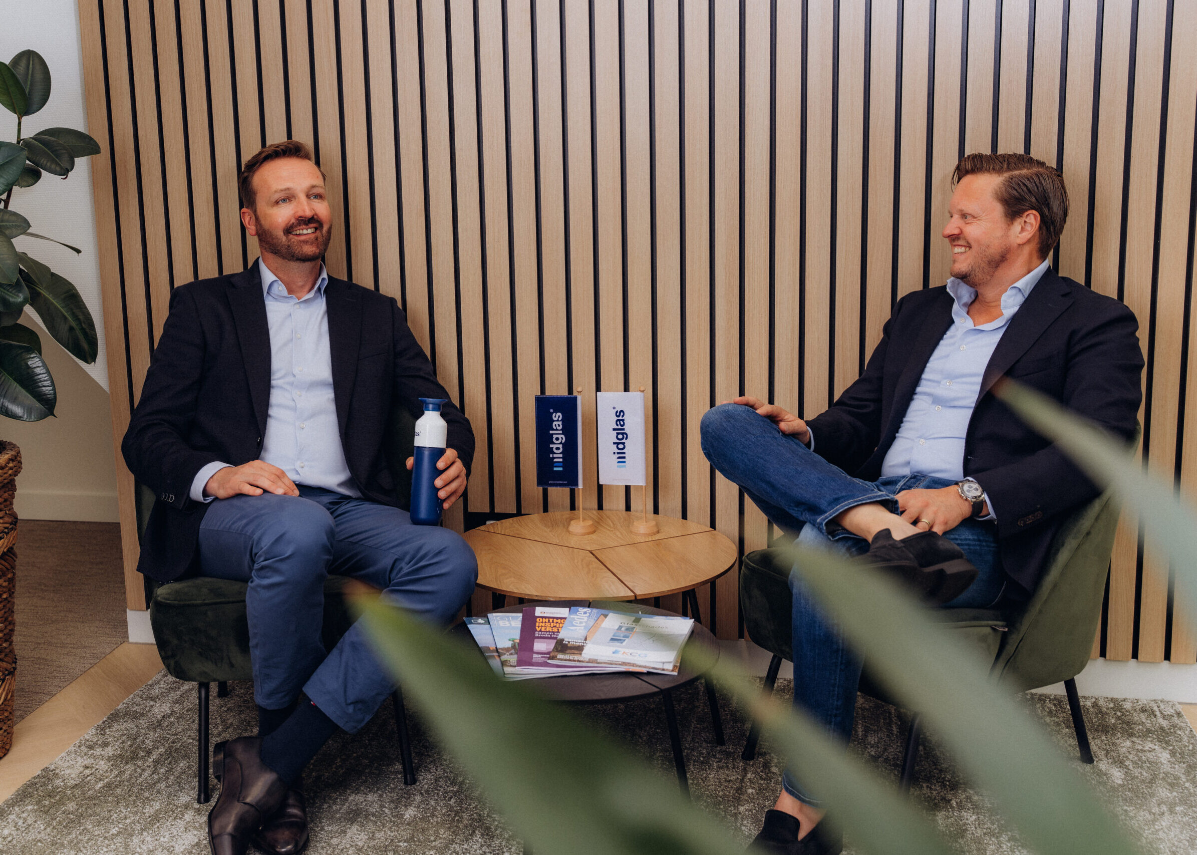 Twee mannelijke Midglas collega's die lachend een gesprek aan het voeren zijn, zittend op stoelen