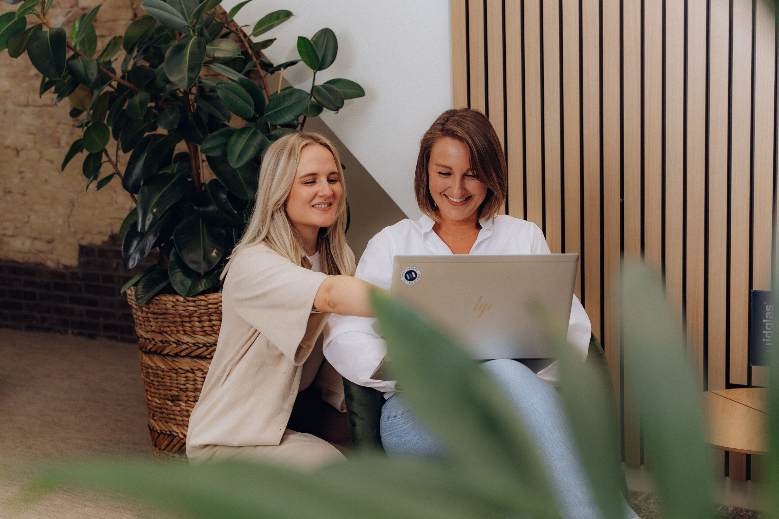 Twee lachende vrouwelijke collega's die samen op een laptop kijken
