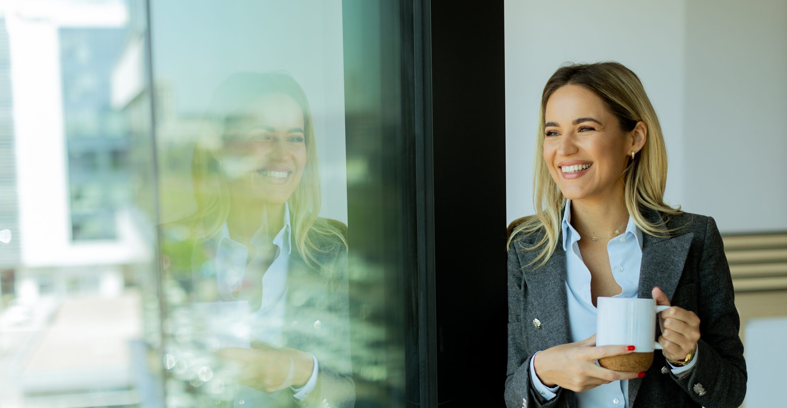 Vrolijke zakenvrouw staand bij een groot raam terwijl ze uitkijkt over de skyline van de stad