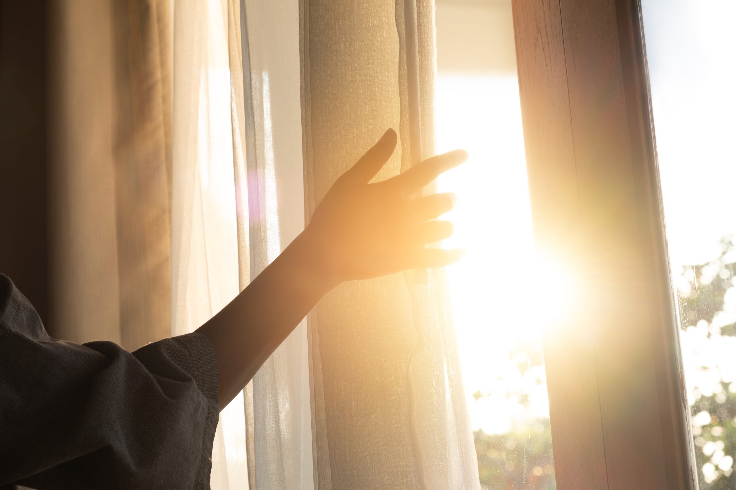 Vrouw die gordijnen open doet waardoor zonlicht binnenkomt