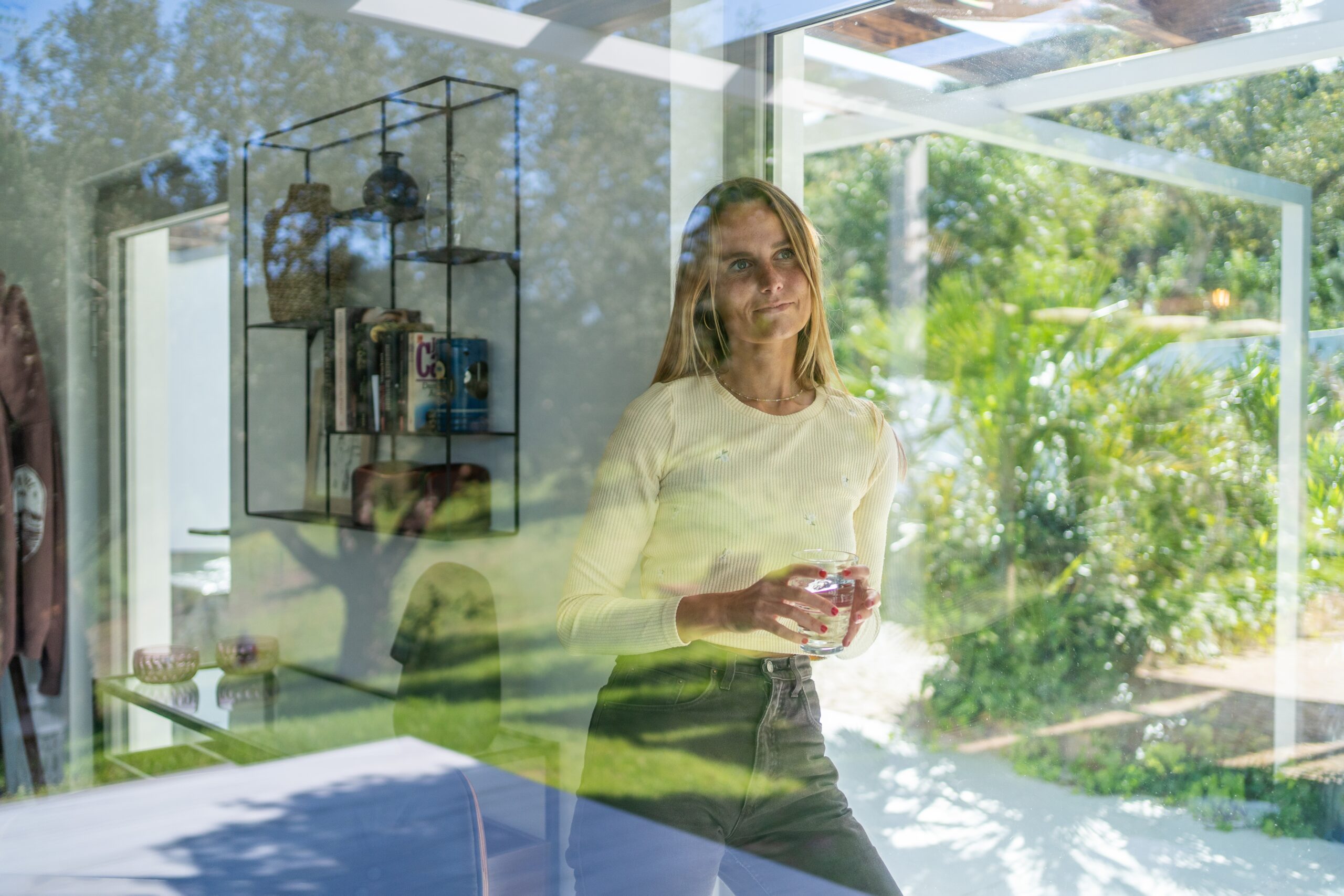 Vrouw kijkt uit het raam bij haar thuis met een kop koffie in de hand